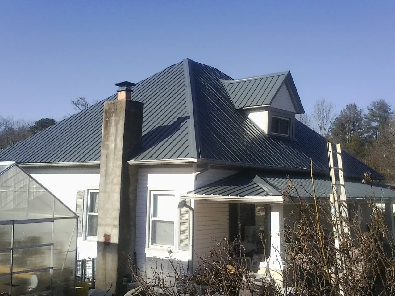 Dark blue standing seam metal roof on a white farmhouse with dormer — Slate & Tile Roof Repair by Roofing Brothers in Saint Leo