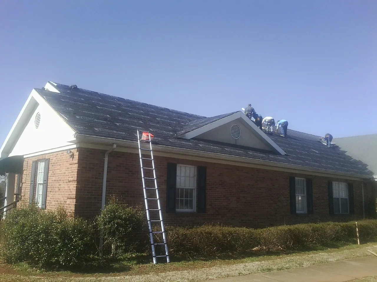 Crew tearing shingles off a brick ranch roof with a ladder set — Emergency Roof Repair work by our crew in Saint Leo