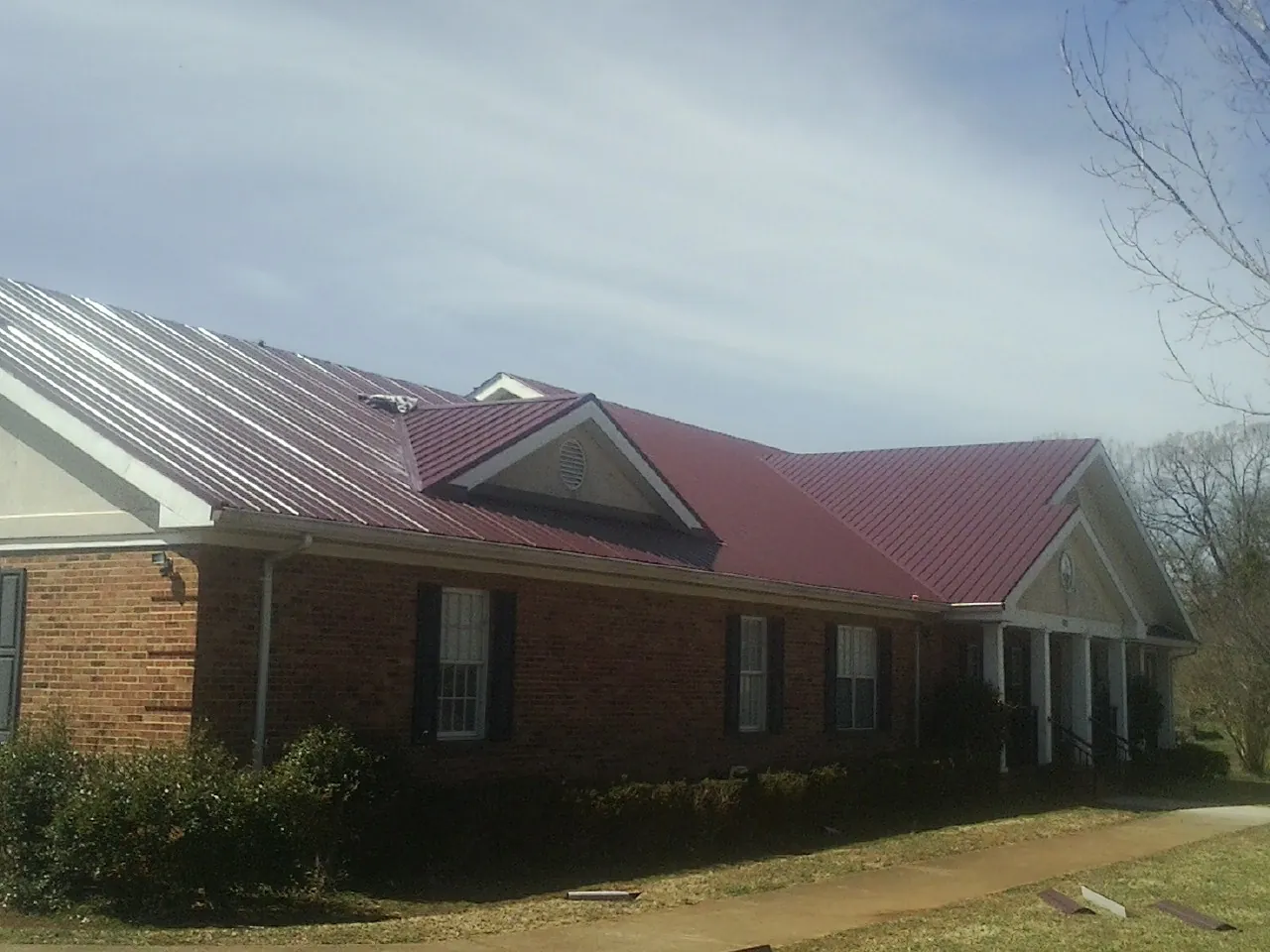 Red metal roof with gabled entries on a long brick building, from a Hail Damage Roof Repair job in Saint Leo