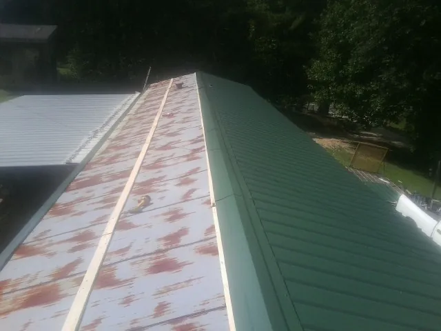 Old rusted panels beside newly installed green metal roofing — Wind Damage Roof Repair by Roofing Brothers in Saint Leo