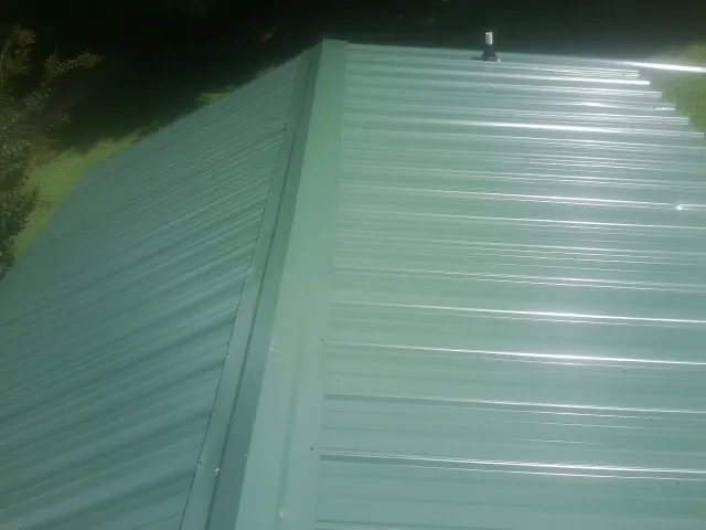 New green metal panels meeting at the ridge of a roof — Flat Roof Repair work by our crew in Saint Leo