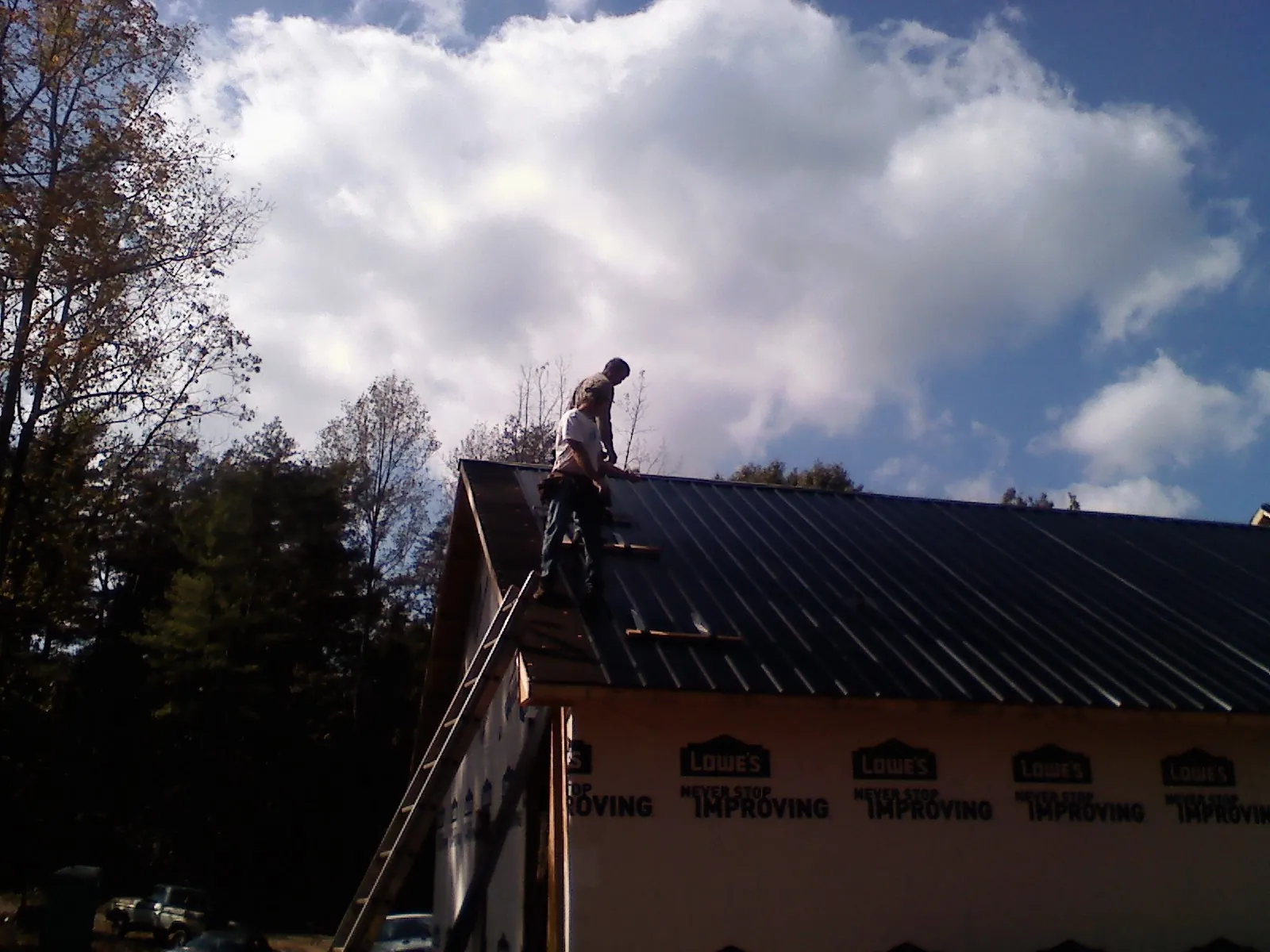 Roofer fastening dark metal panels high against a cloudy sky, from a Roof Inspection job in Saint Leo